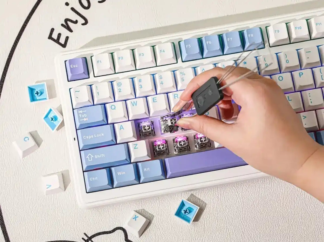 Hand using a keycap puller to remove blue and purple keys from a white mechanical keyboard.