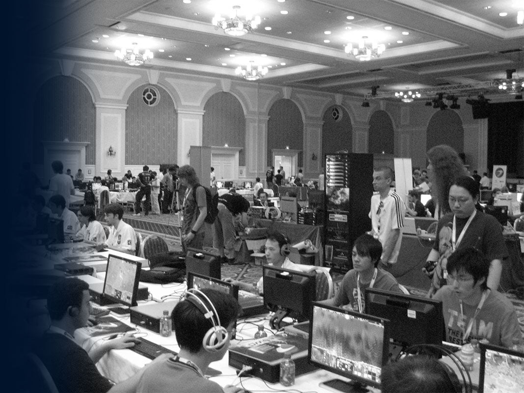 Large-scale esports or LAN party event photo in a convention hall, showing many gamers with computers and headsets.