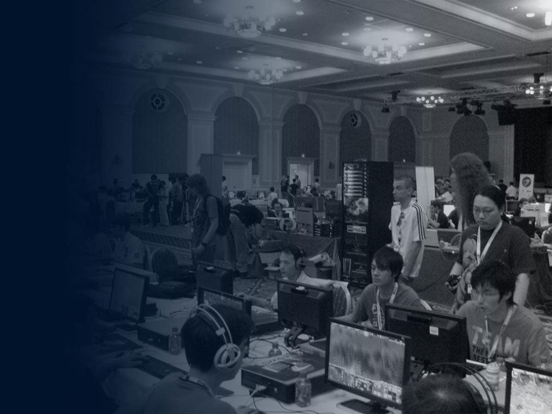 Black and white photo of a large LAN gaming event with multiple participants playing on desktop computers in a spacious ballroom or convention hall.