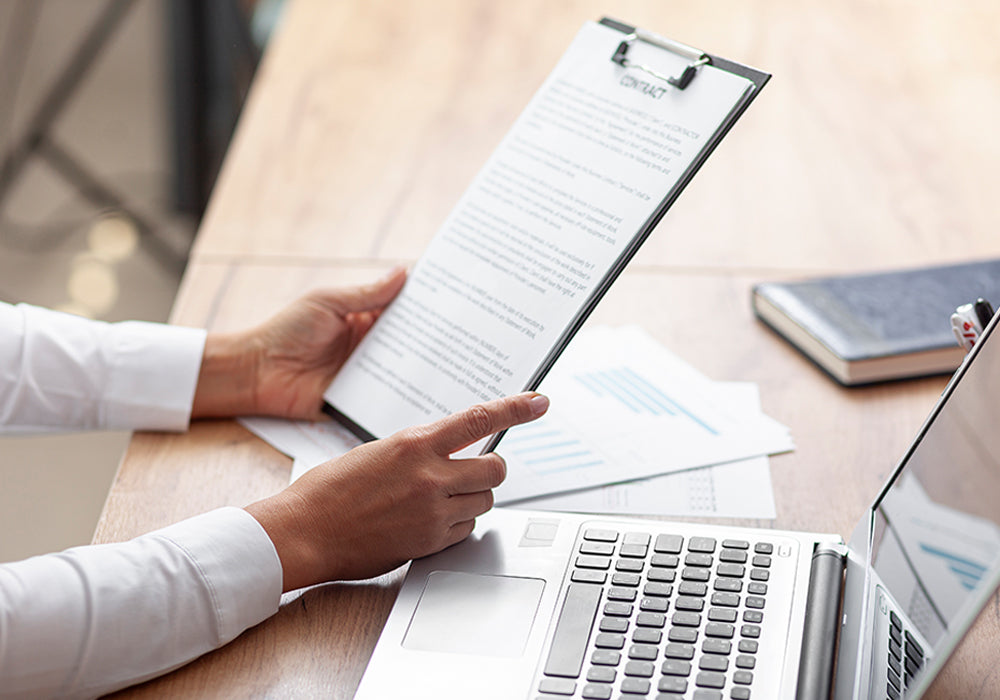 Person holding a document next to a laptop on a desk
